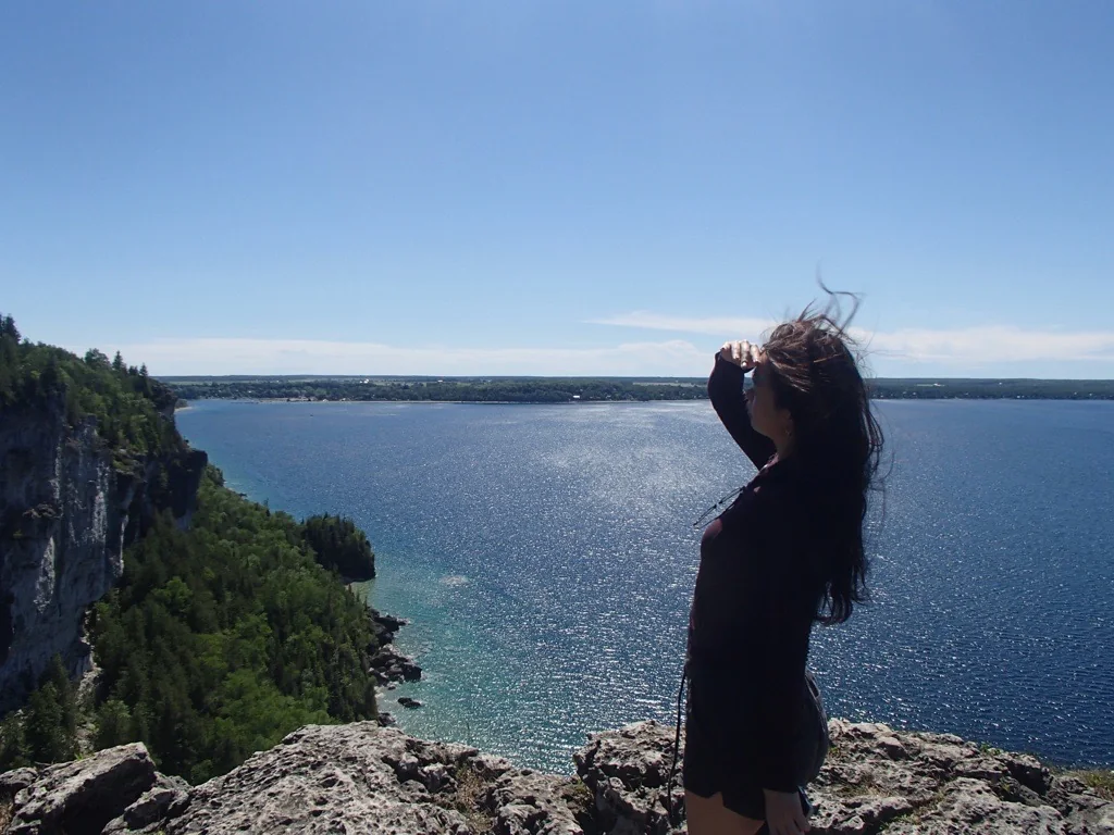 Amanda at a windy cliffside overlooking a wide blue lake