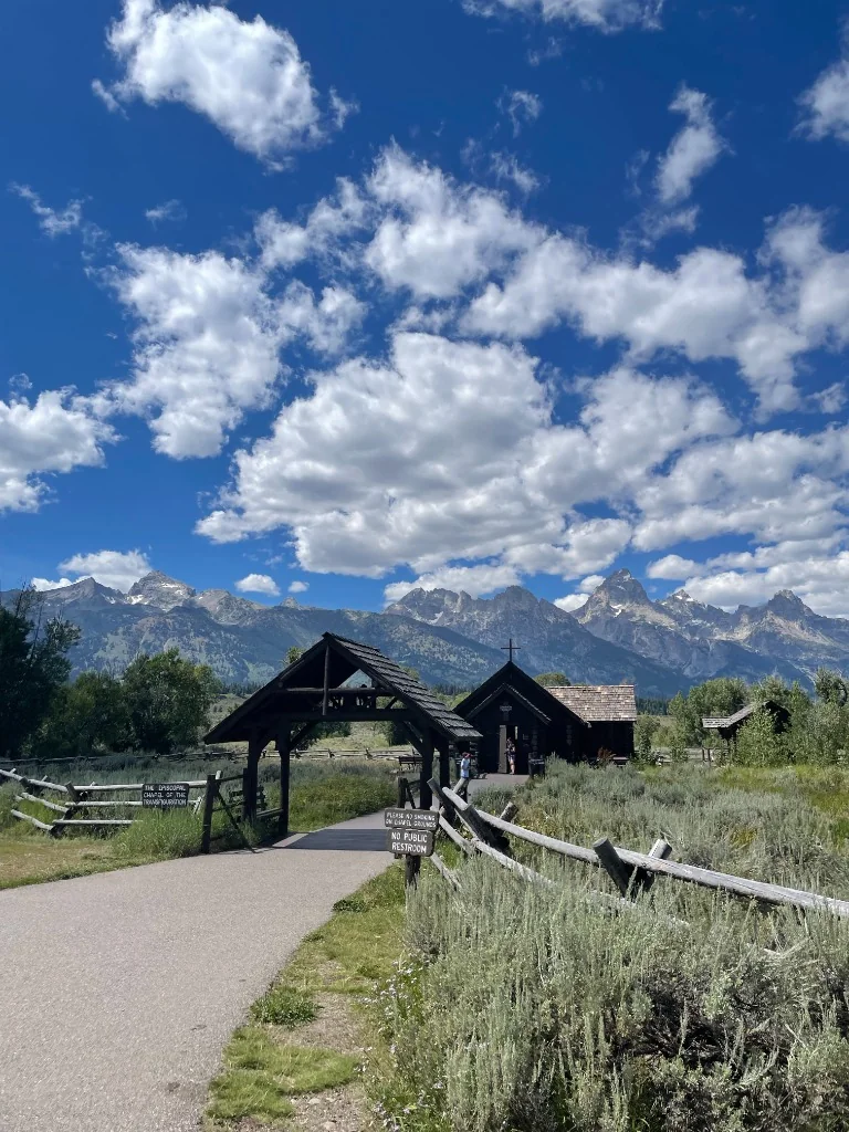 A small wooden chapel beneath a mountain range and bright clouds
